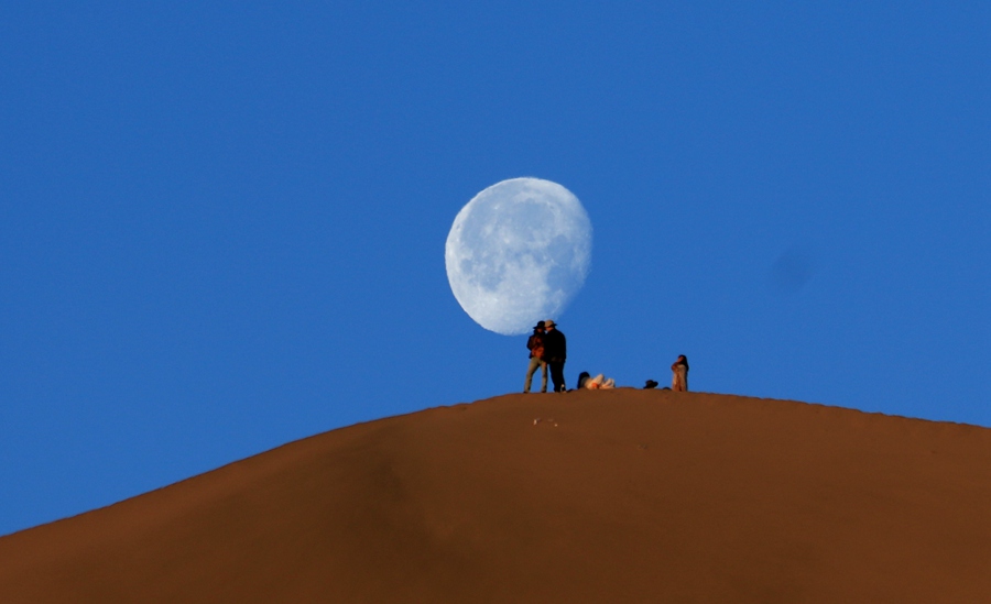 6月7日清晨，游客在甘肅省敦煌市鳴沙山山頂賞月。張曉亮攝