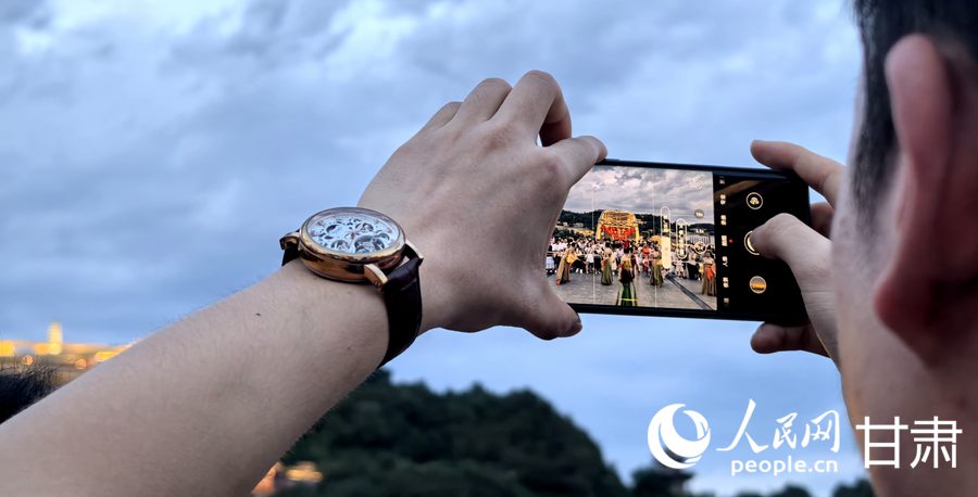 一位游客用手機拍攝中山橋頭的敦煌舞舞者。