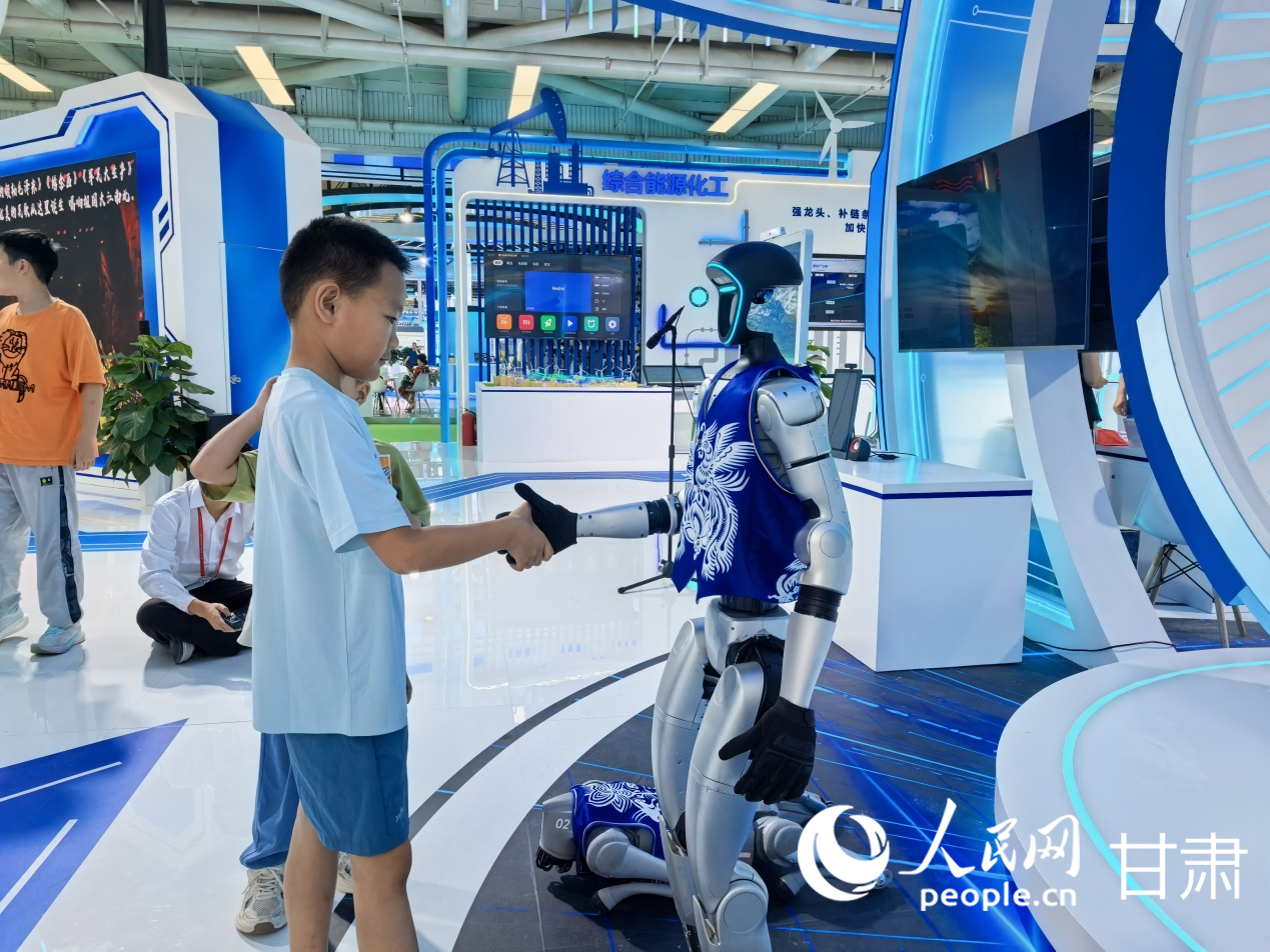 第三十一屆蘭洽會慶陽展館內，身著非遺剪紙服飾的機器人正與小朋友握手。人民網記者 高翔攝